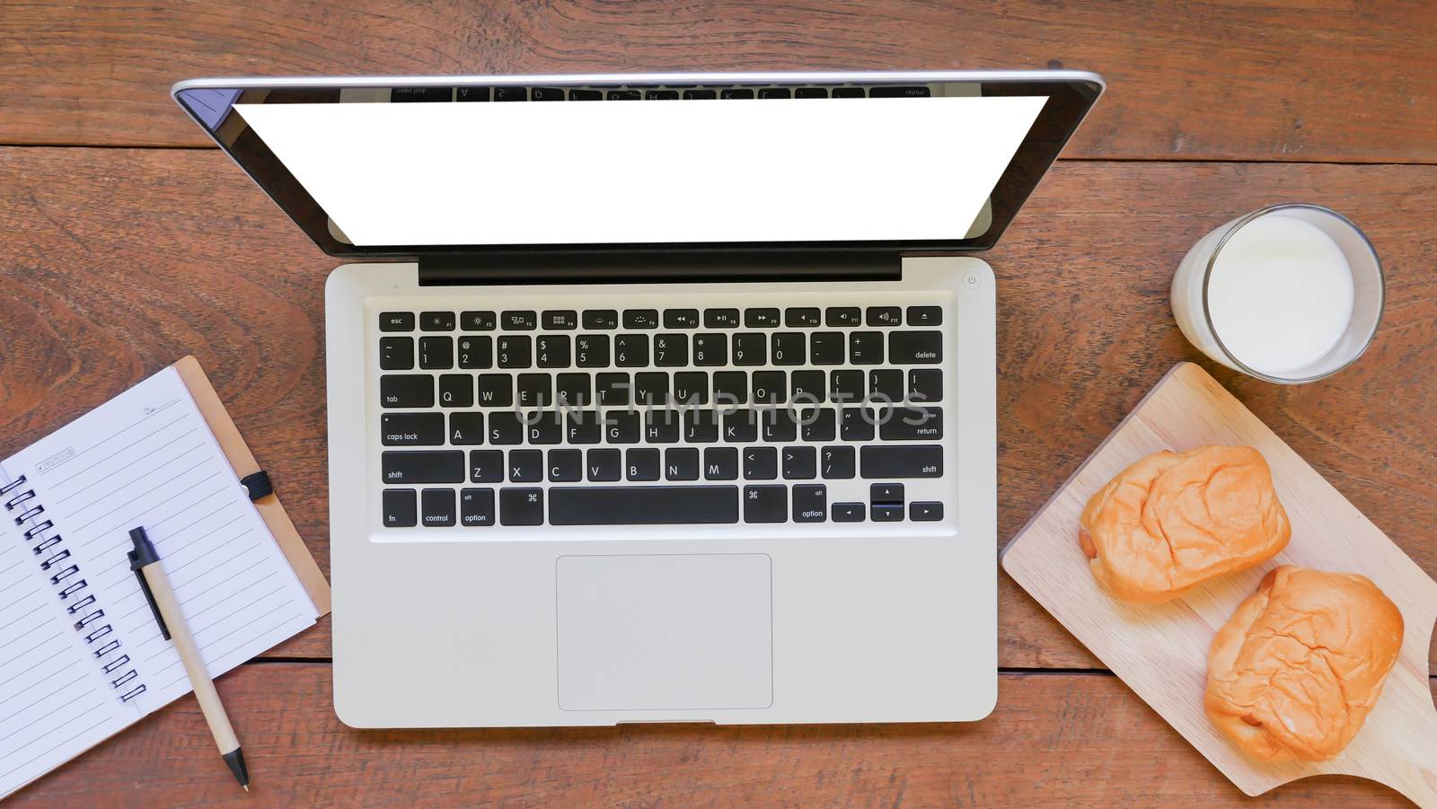 Notebook with labtop,bread and cup of milk on wooden table background.