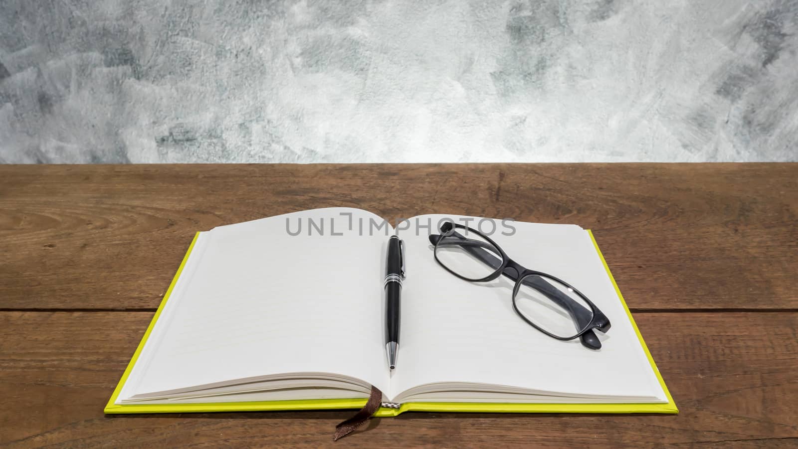 Blank notebook with pen and glasses on wooden table.
