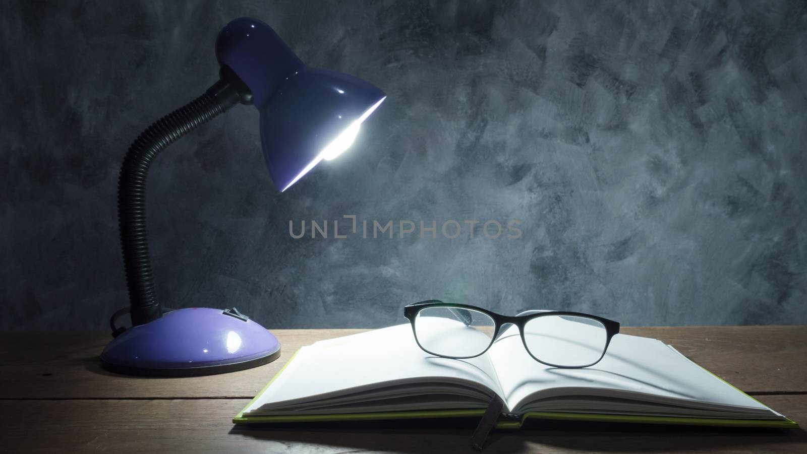 Lamp with notebook and glasses  on  wooden table with vintage wall background.