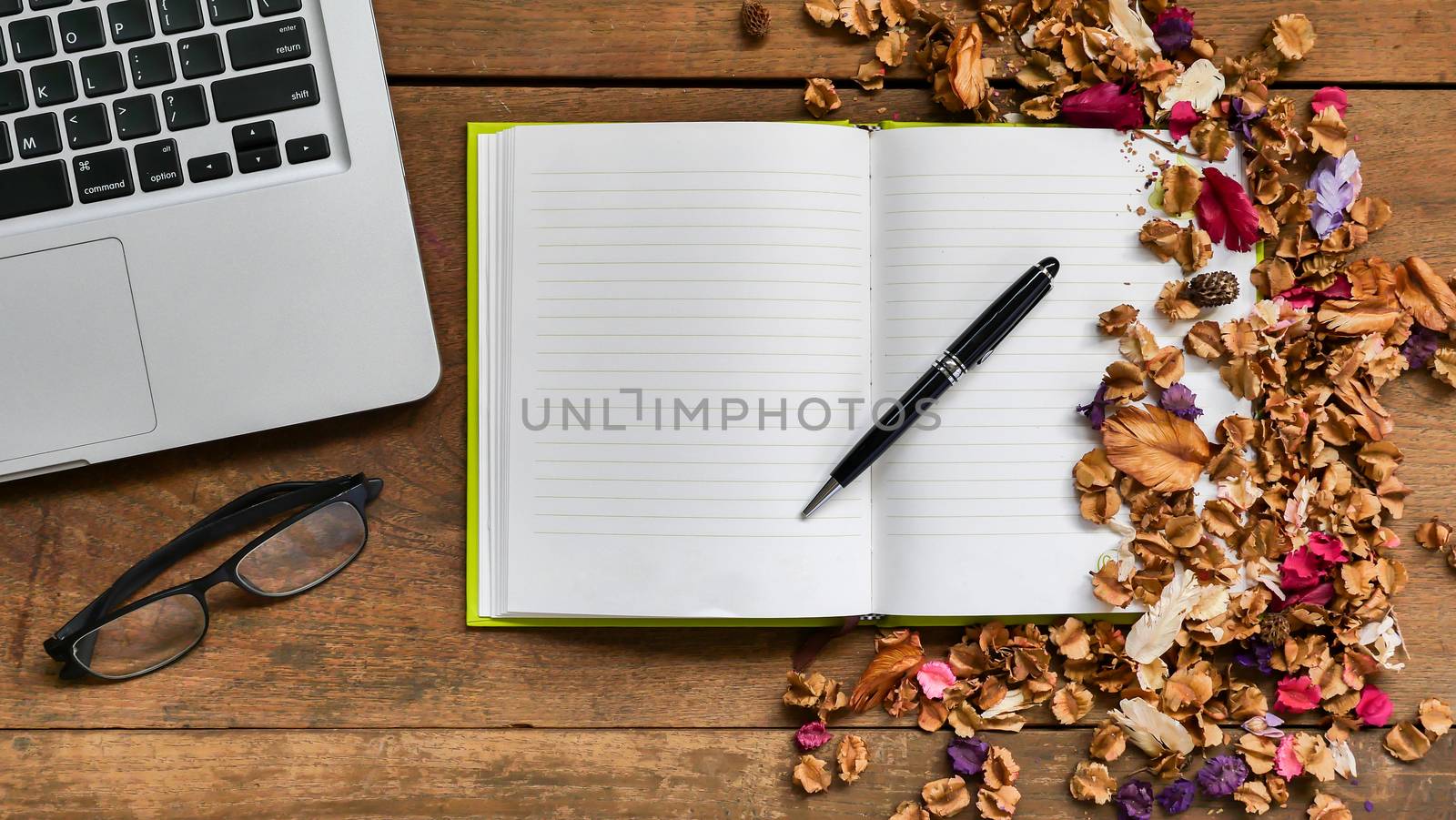 Top view workspace with notebook,pen,glasses,laptop and dried fllowers on wooden table background . by ronnarong