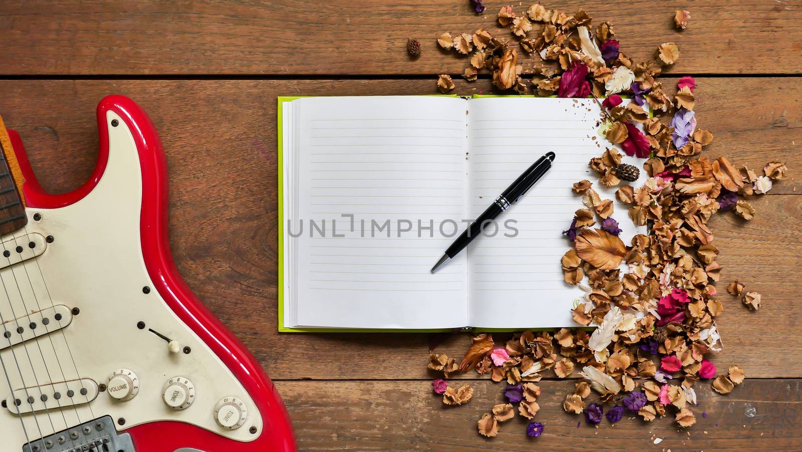 Top view workspace with notebook,pen,electric guitar  and dried flowers on wooden table background .