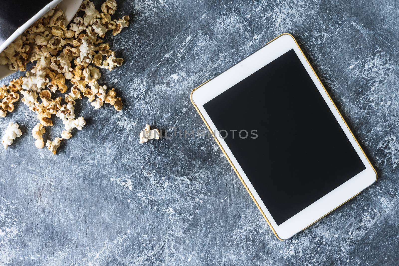 White tablet touch computer gadget with popcorn on grunge background.