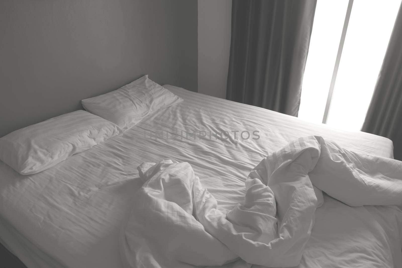 Messy white bedding sheets and pillows. black and white tone by ronnarong