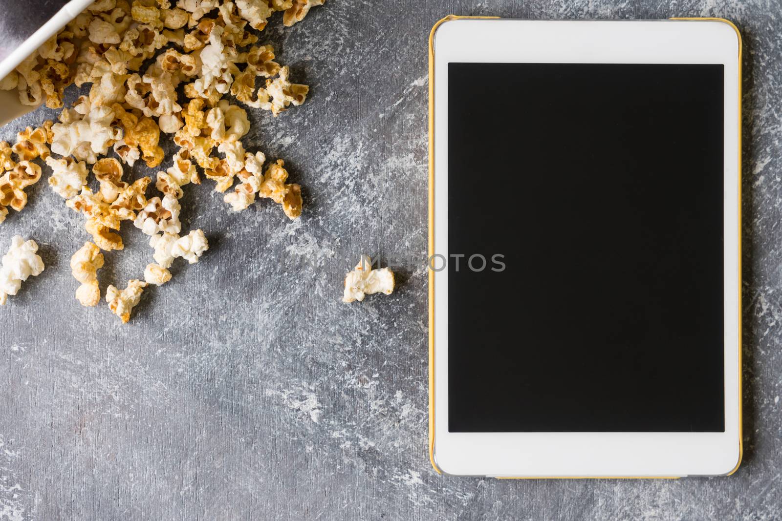 White tablet touch computer gadget with popcorn on grunge background.