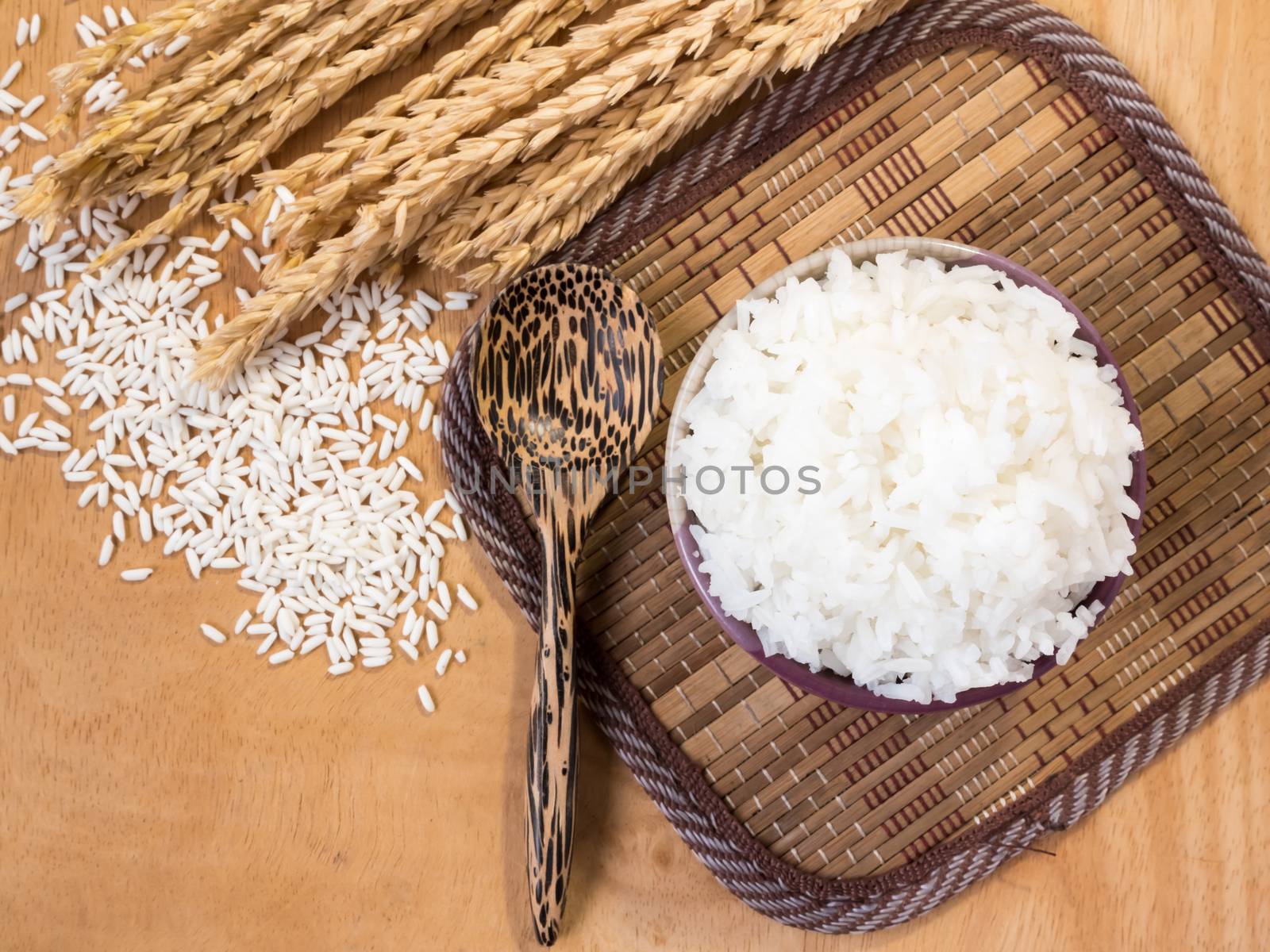 Cooked rice in bowl with raw rice grain and dry rice plant on wooden table background. by ronnarong