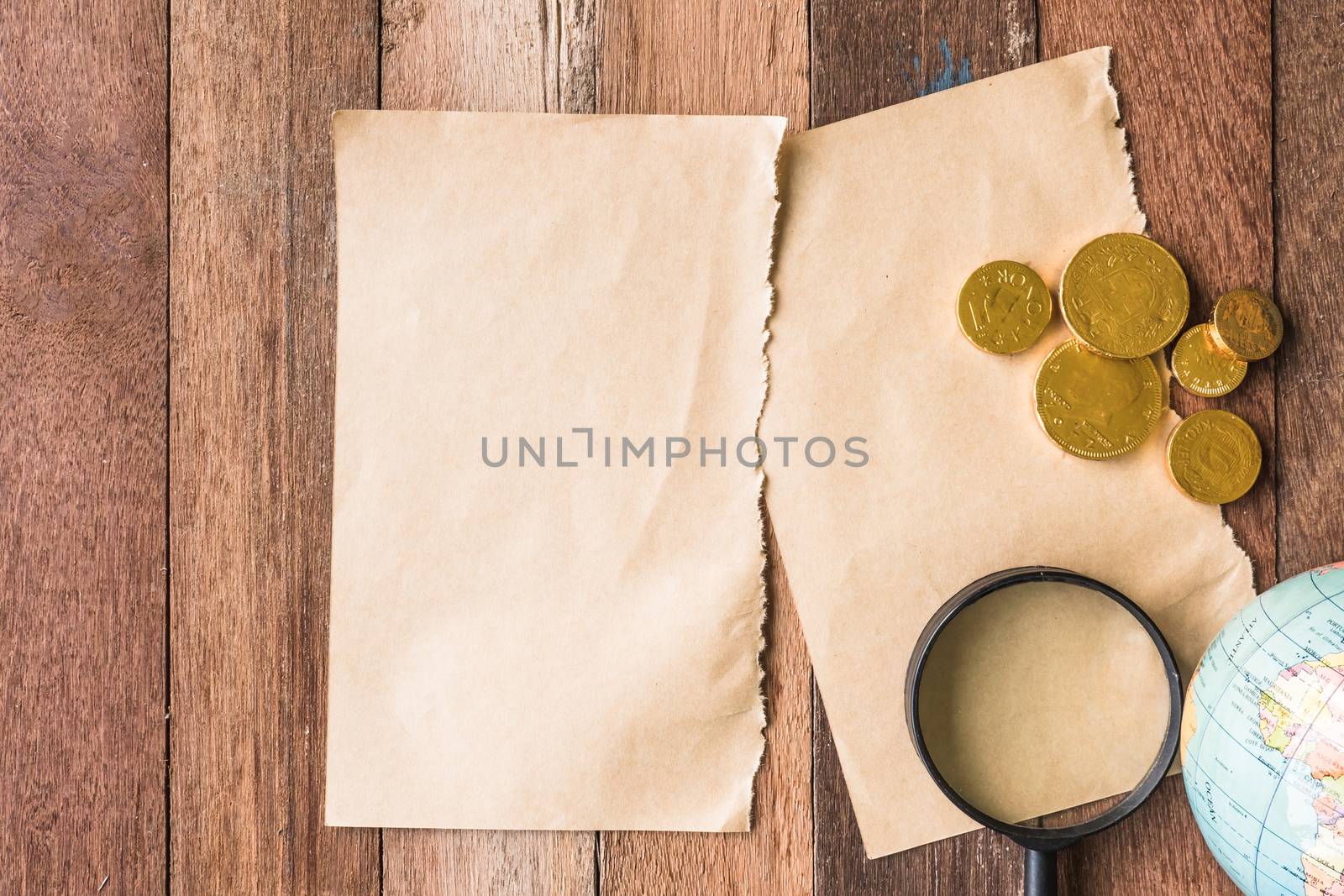 Top view of Blank brown paper with coins, Magnifier and globe on wooden table background.