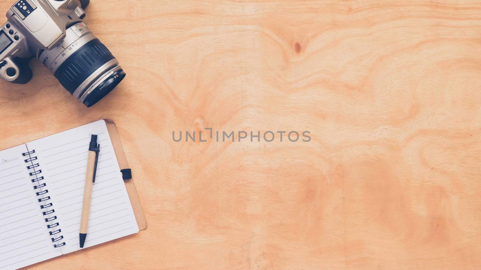 Top view of camera with notebook and pen on wooden table background.