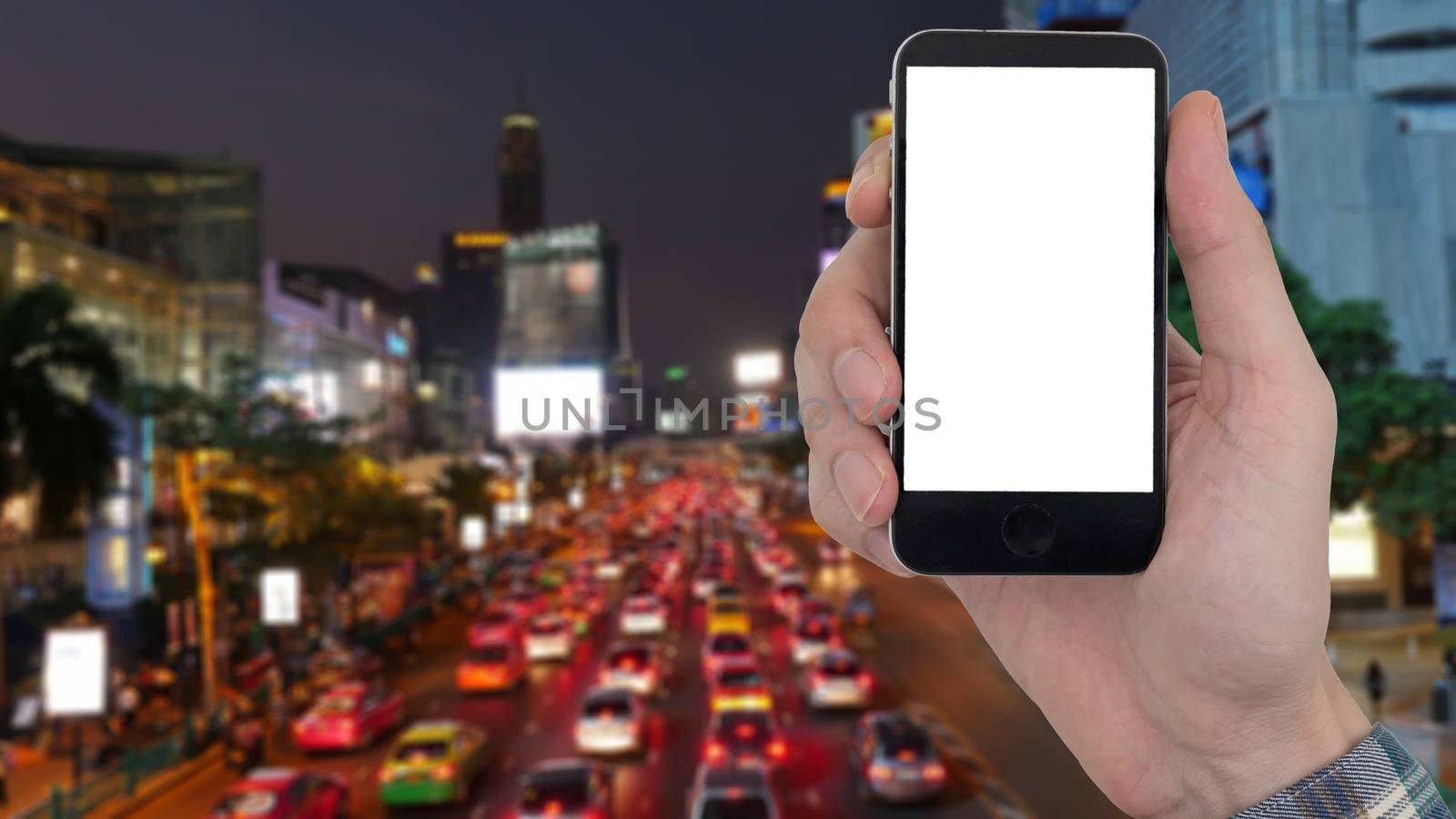 Male hand holding a mobile phone with touch blank white screen on blurred city landscape background.