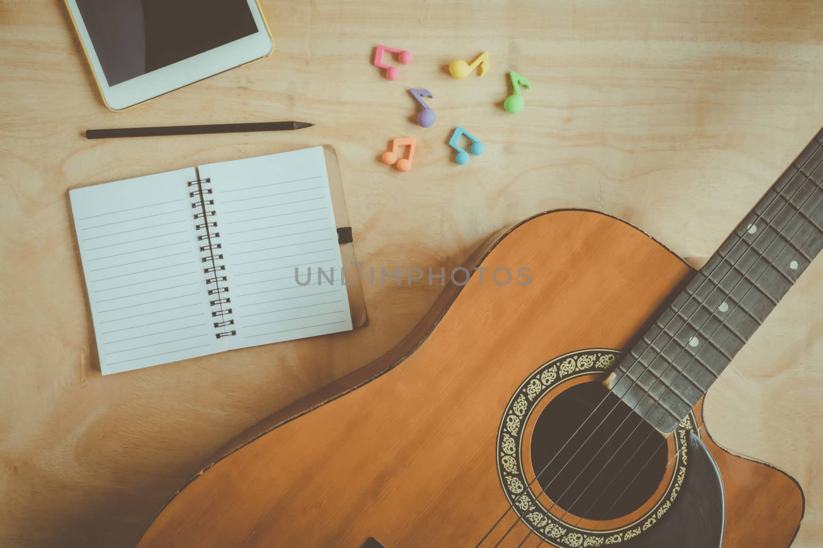 Top view of acoustic guitar with blank notebook on wooden table background.vintage effect style picture