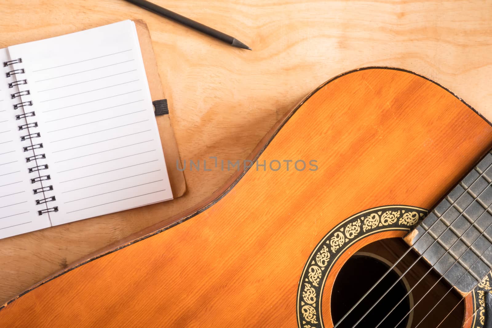 Top view of acoustic guitar with blank notebook on wooden table background.