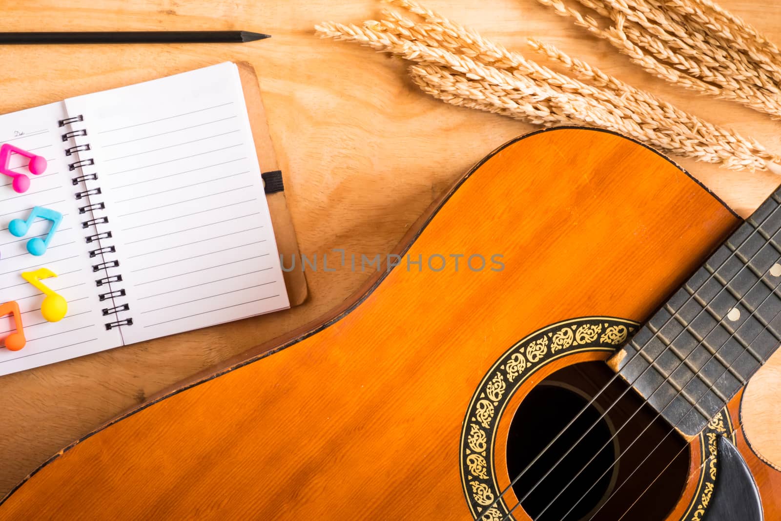Top view of acoustic guitar with blank notebook on wooden table background.
