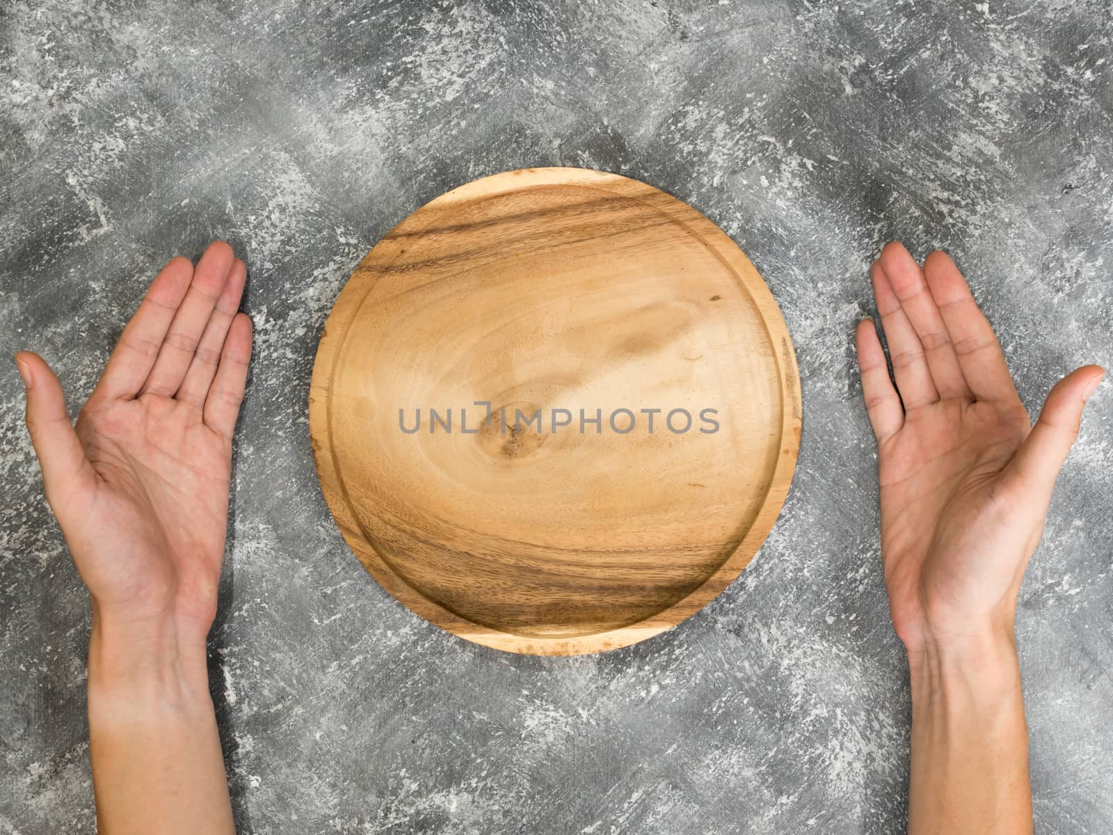 Top view of empty wooden tray with hands on grunge  background.