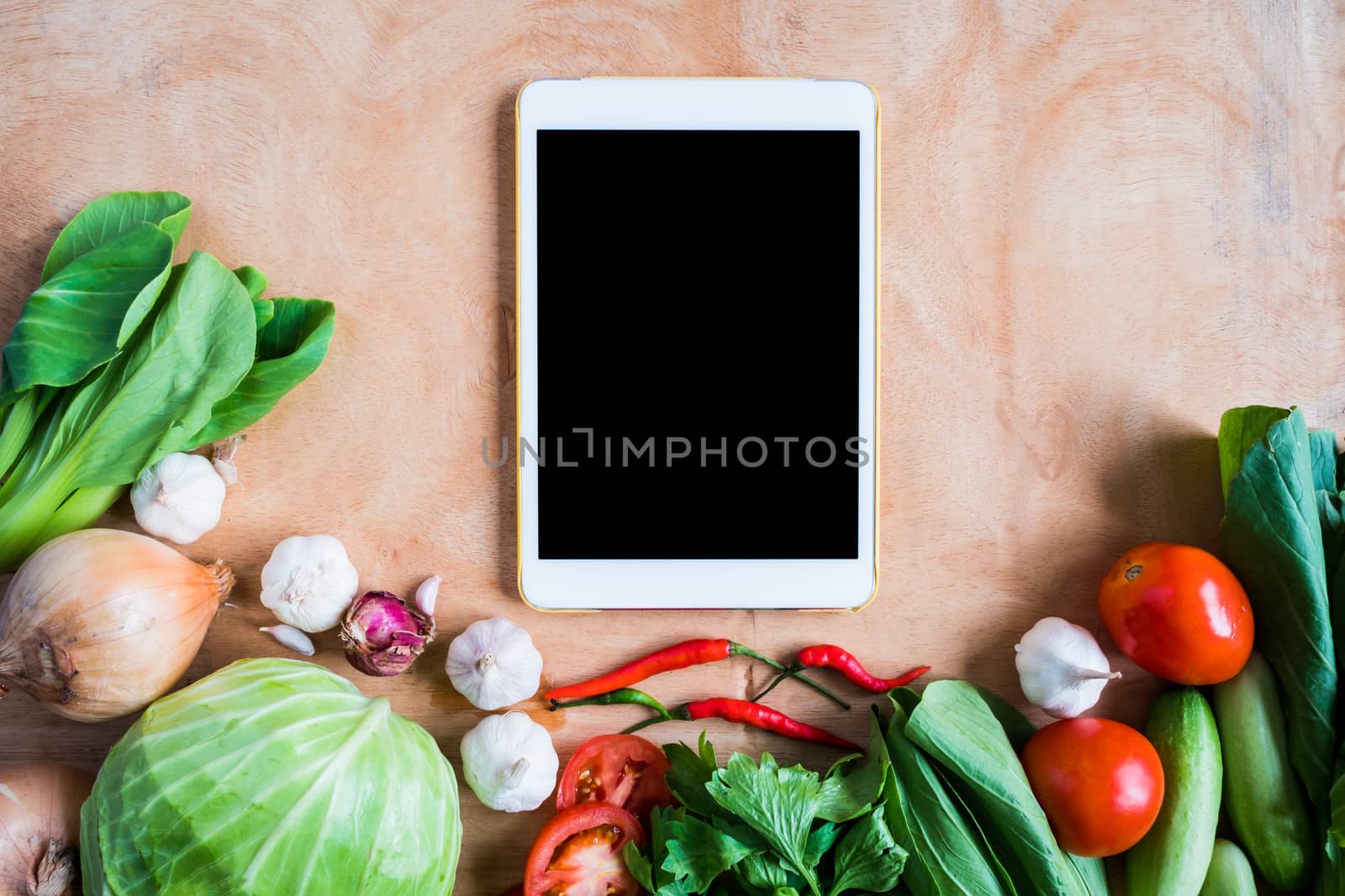 Top view of Fresh vegetables with tablet touch computer gadget on wooden table background.