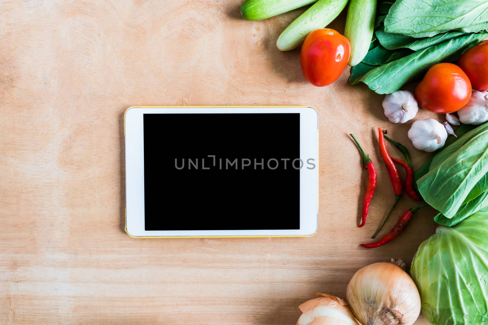 Top view of Fresh vegetables with tablet touch computer gadget on wooden table background.