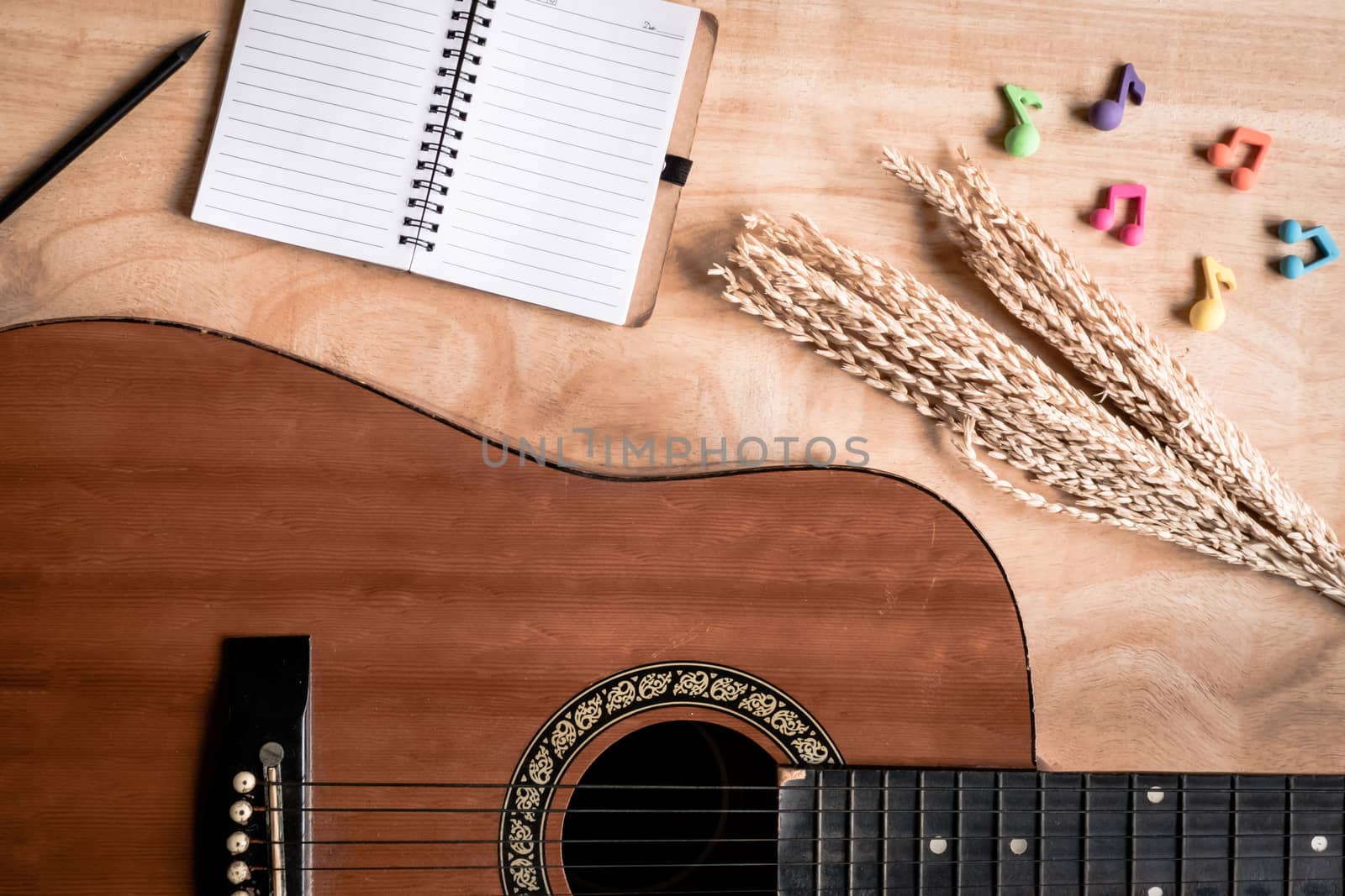 Top view of acoustic guitar with blank notebook on wooden table background.