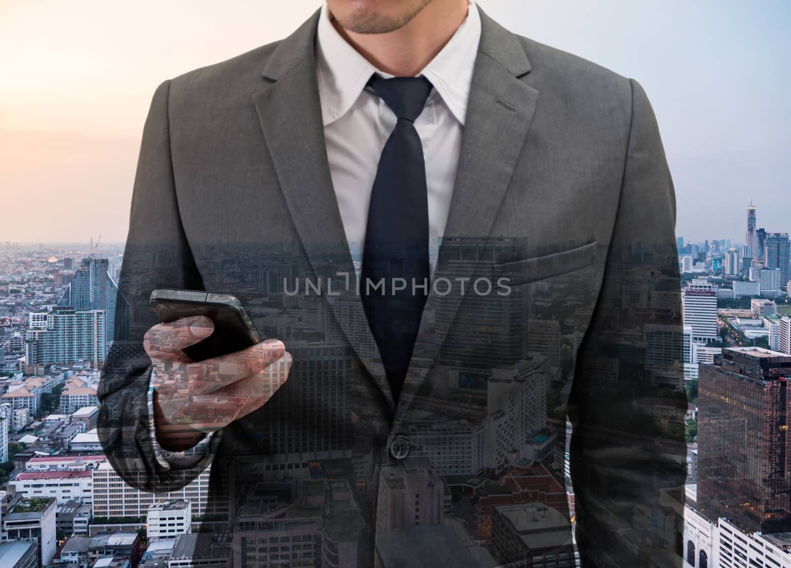 Double exposed of Businessman holding mobile phone with cityscape.