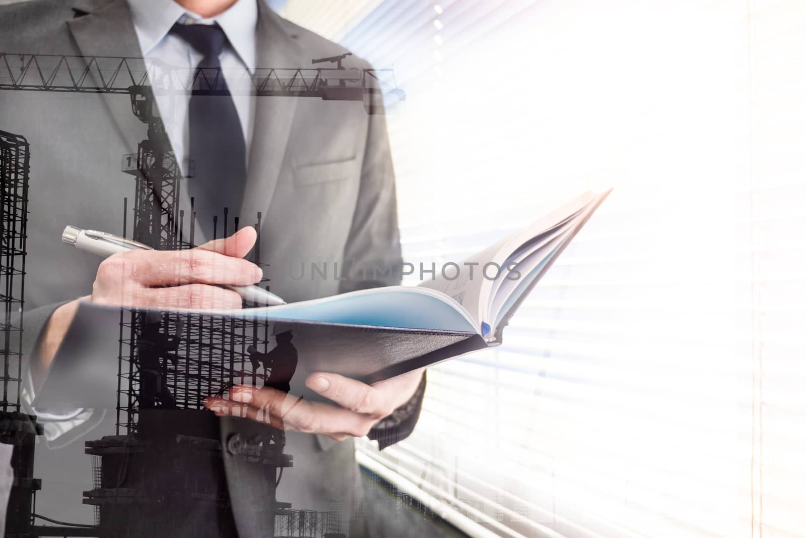 Double exposed of businessman writing some data in notebook with the building construction site.