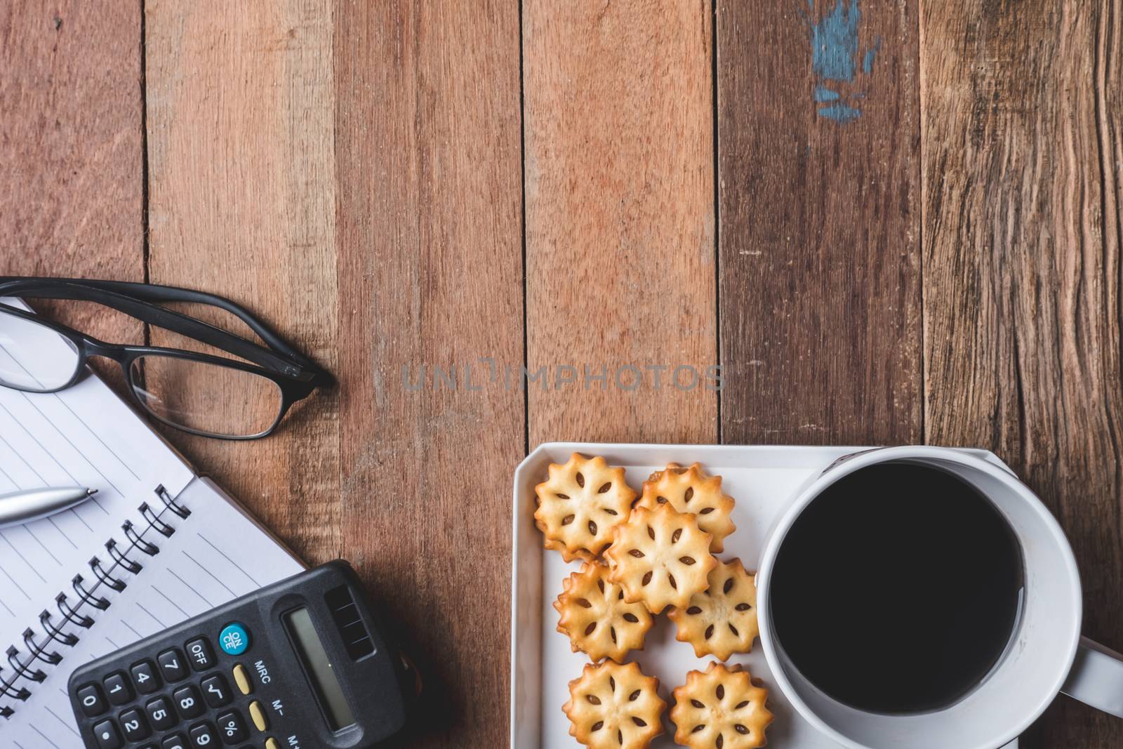 Top view of Notebook with glasses,cookie and coffee cup on wooden table background. Free space for text