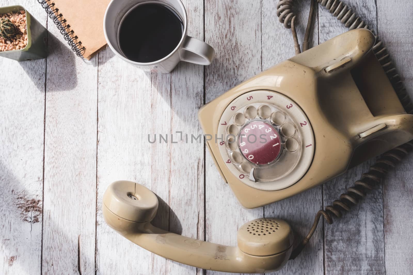 Top view of Old telephone with coffee cup,notebook and cactus on white wooden table background.
