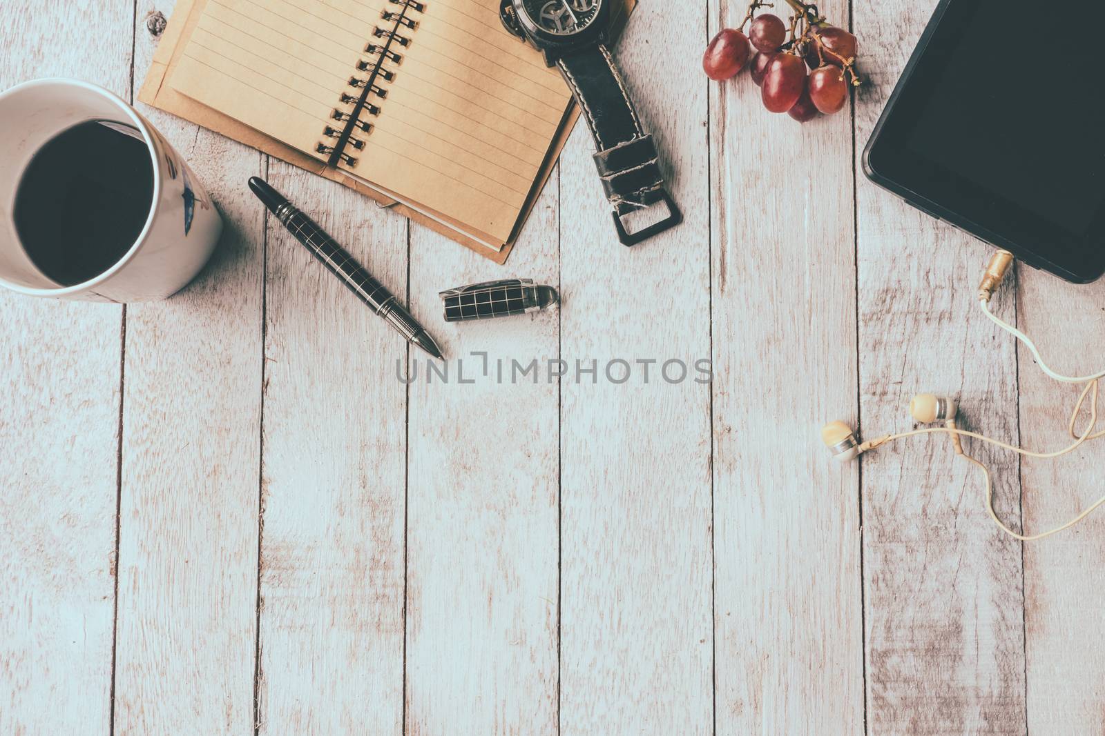 Top view of Coffee cup with notebook,pen,watch,tablet,earphone and grape on white wooden table background, Vintage tone, Free space for text