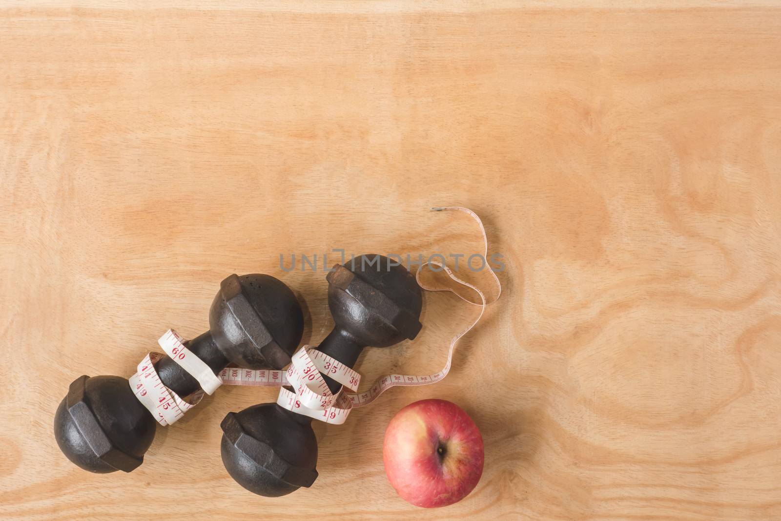 Top view of iron dumbbells with measure tape and apple on wooden table background. Free space for text