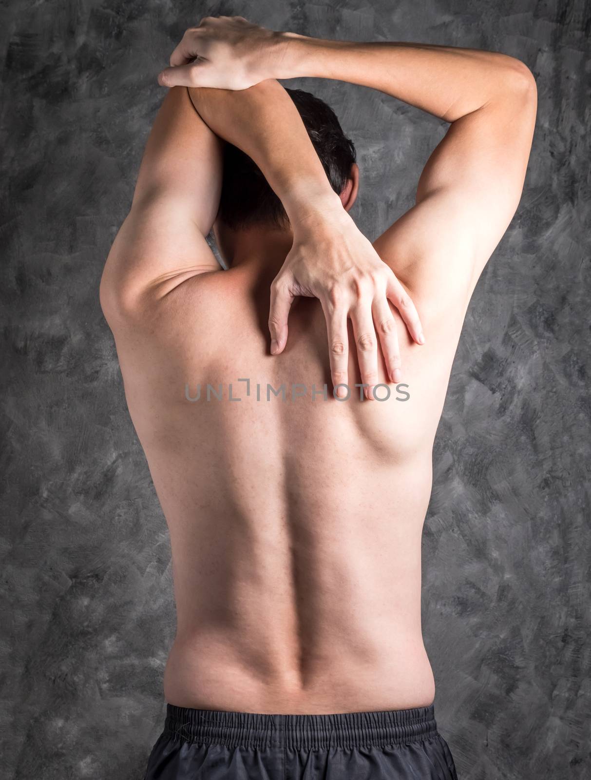 A man performing triceps stretch on grey background.