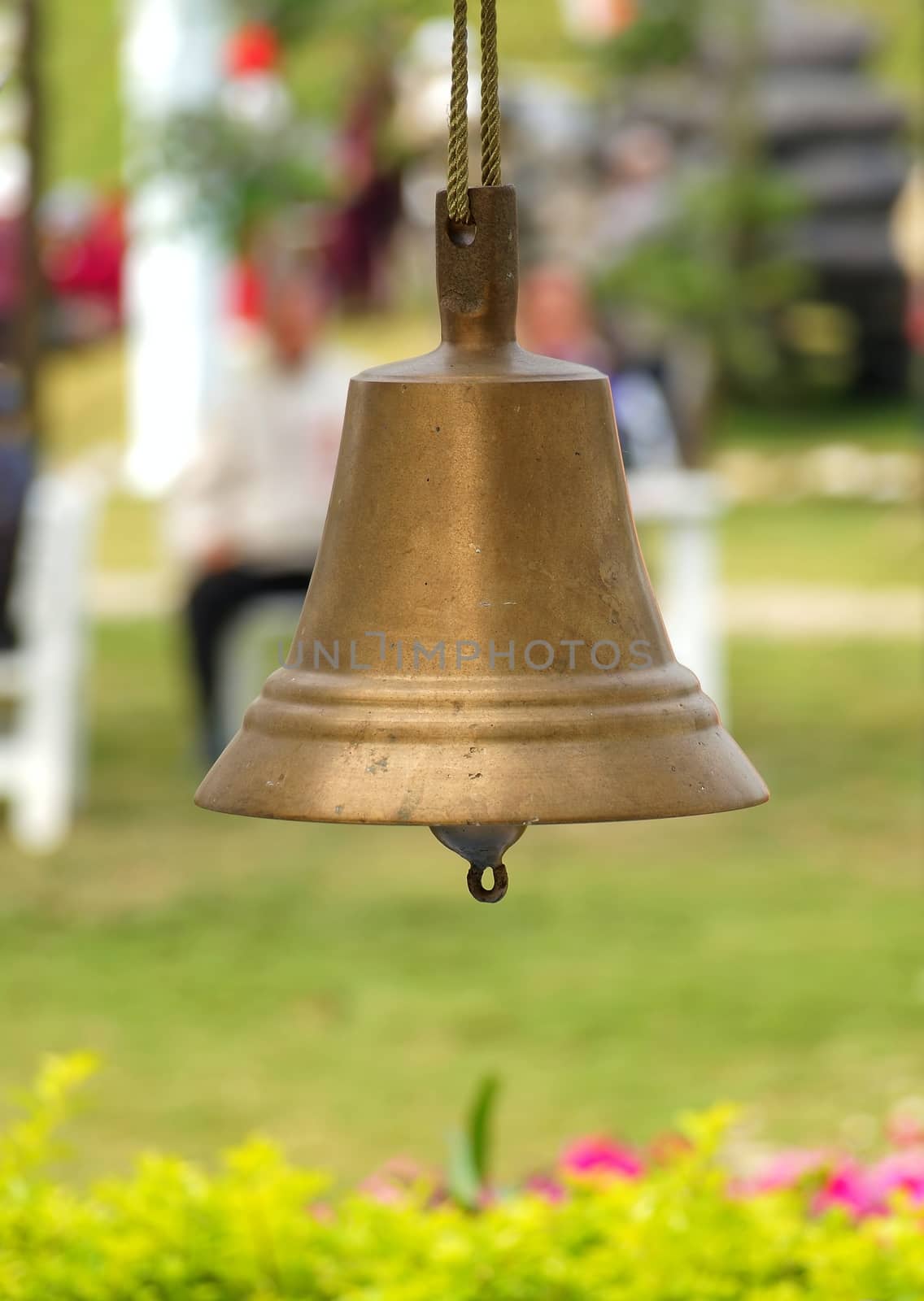 A bronze bell suspended from a rope hangs in a nice garden
