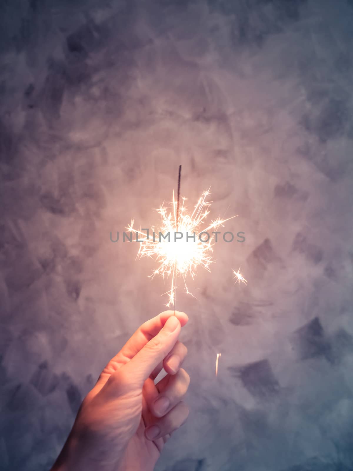 Close up of hand holding sparkler on grunge background by ronnarong