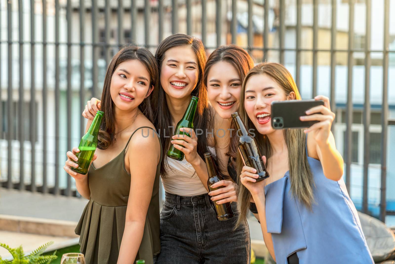 Happiness Asian Girl Friend Group taking a selfie while celebrating and dancing together with her beer bottle at sunset time on rooftop, hens night, holiday, or yearly anniversary party concept