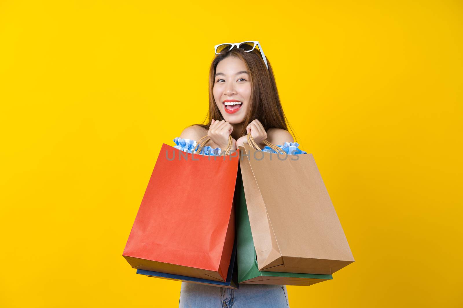 Attractive Asian smiling young woman Carrying shopping coloful bag on aisolated yellow color background, copy space and studio, black friday season sale concept.