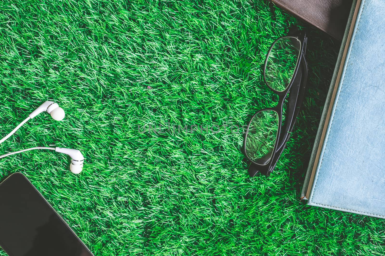 Top view of books with glasses, smart phone and earphones on green grass background.