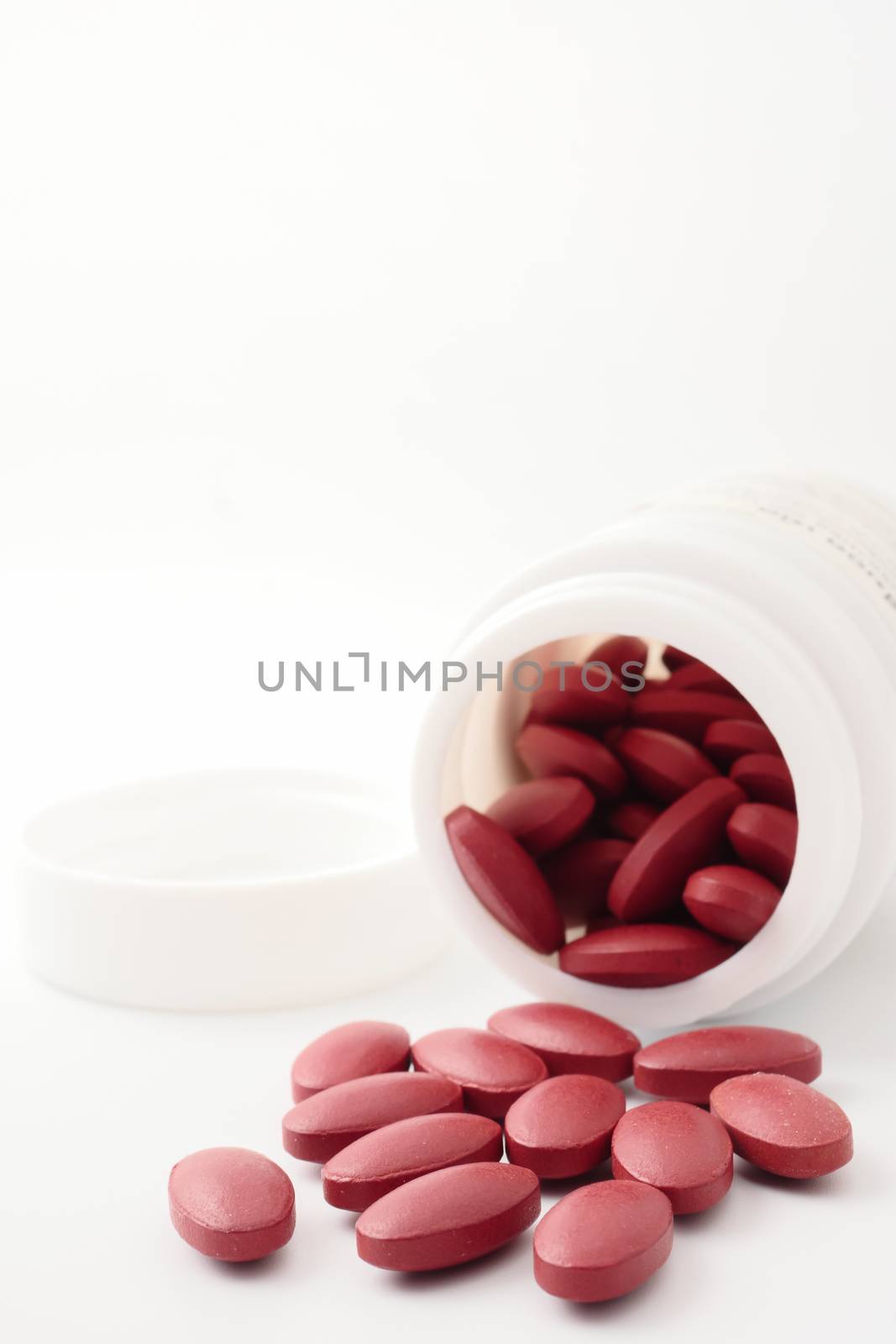 Red vitamin pills pouring out of the bottle on white background.