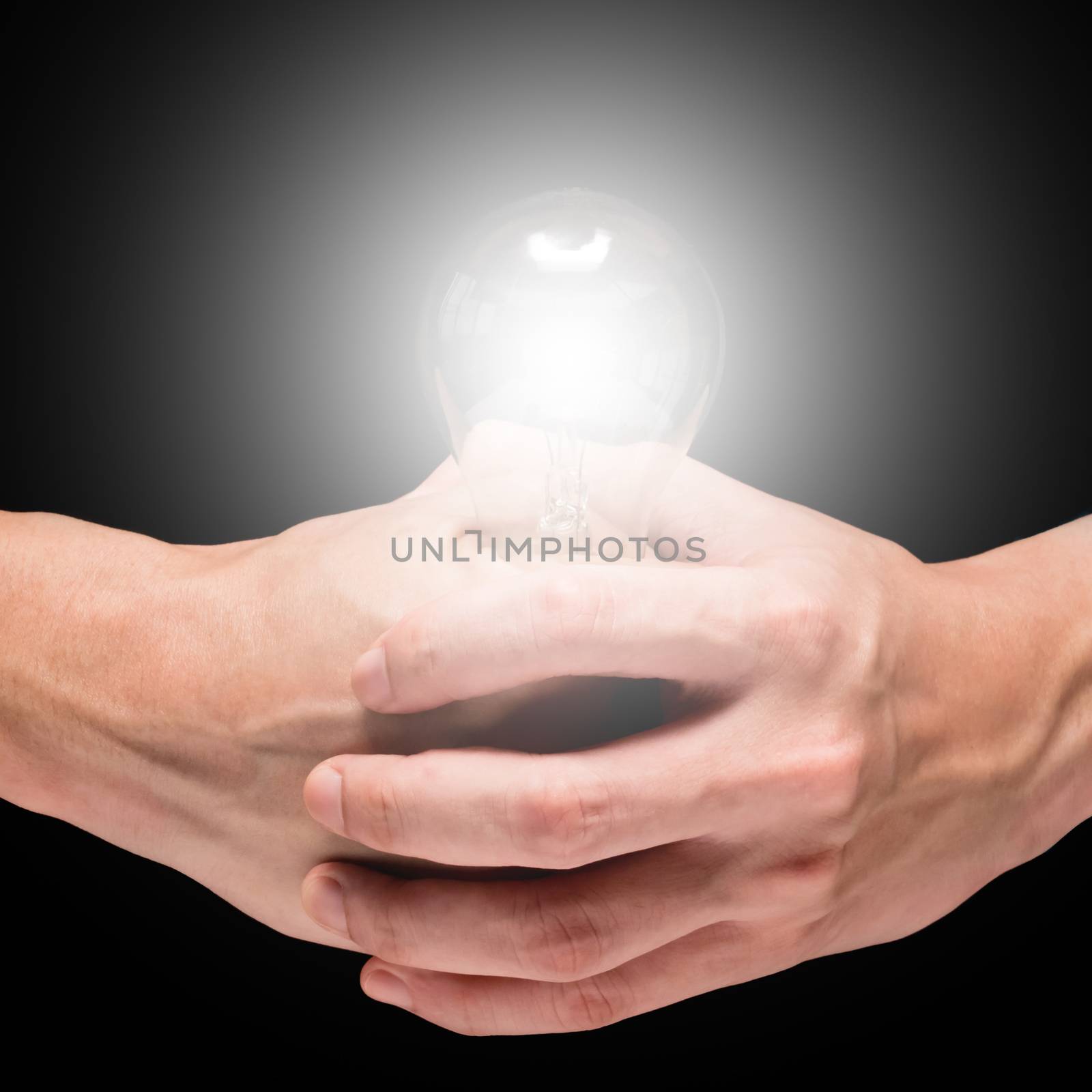 Male hands holding light bulb on a black background.
