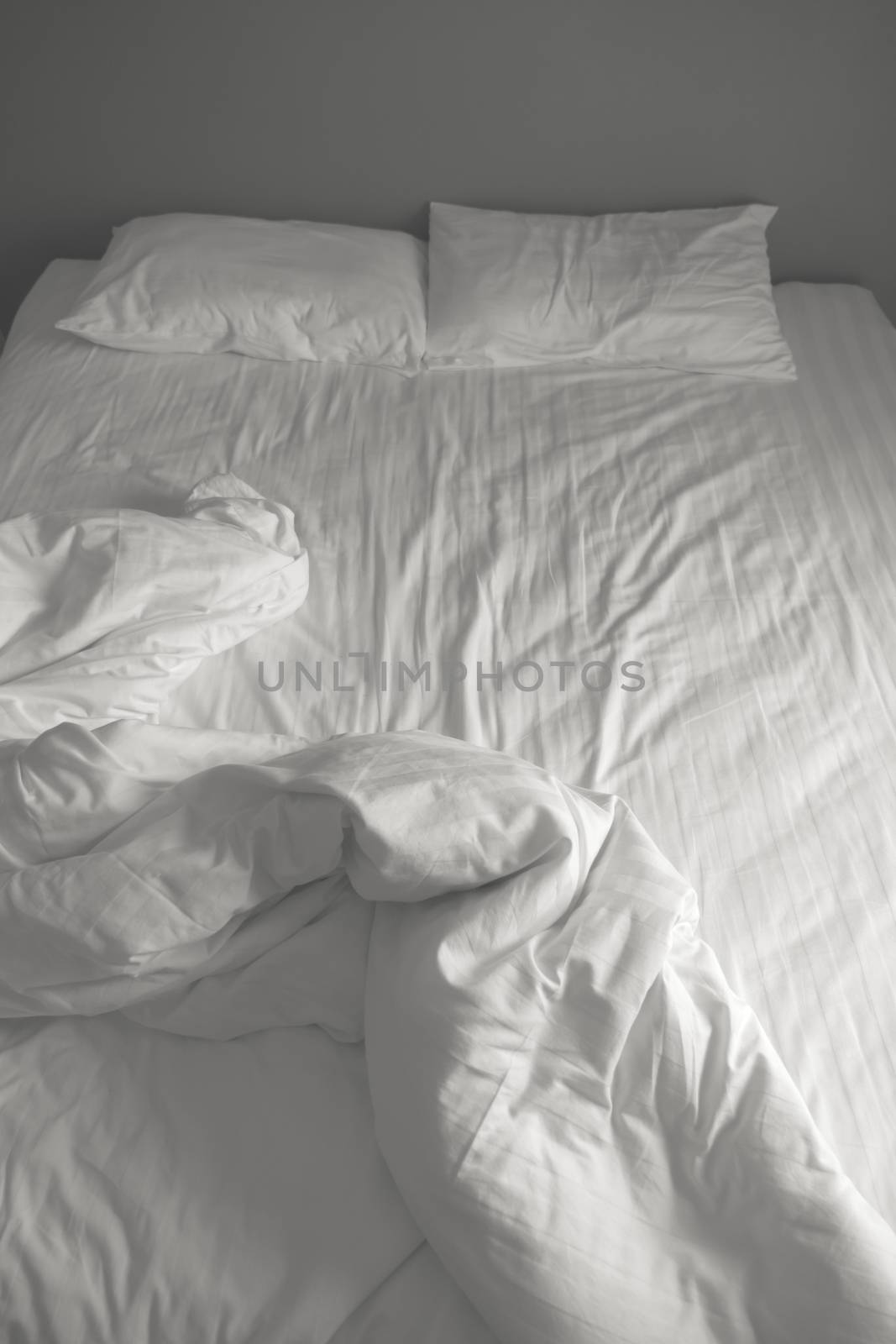 Messy white bedding sheets and pillows. black and white tone by ronnarong