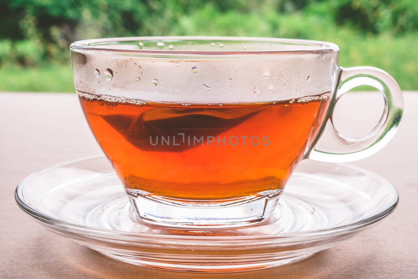 A cup of tea on the wooden table, tea bag in glass, nature background.