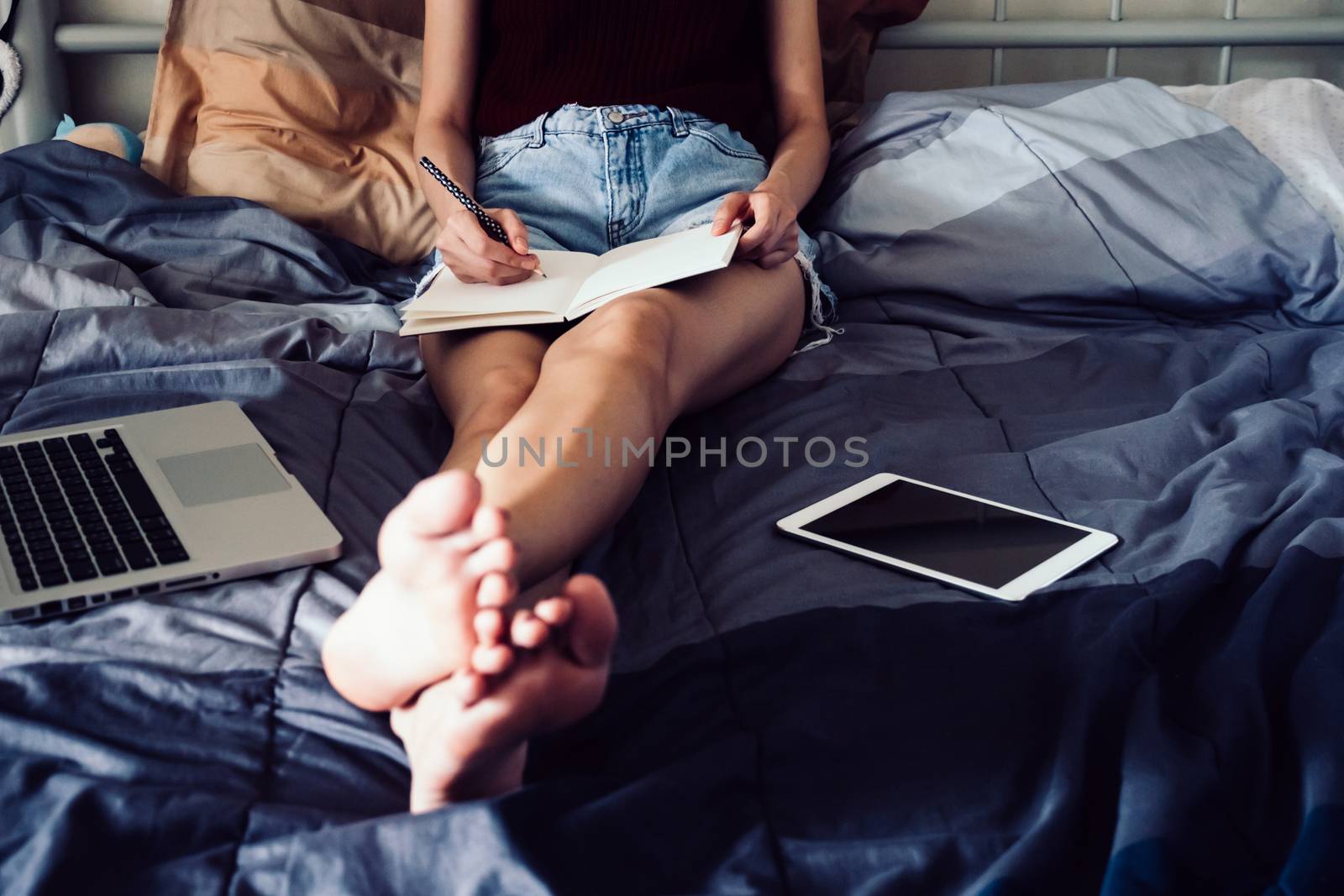 Close up of young woman writing in a book while sitting on her bed, Films grain filter.