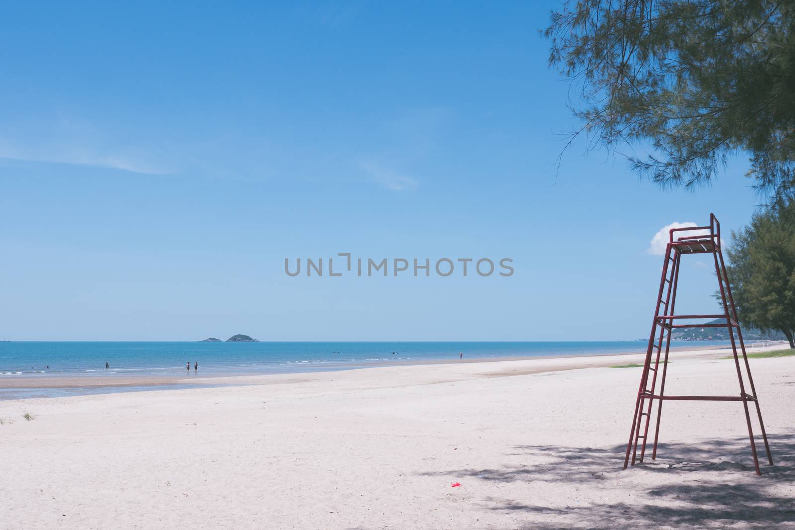 Beautiful beach with blue sky and a tall red lifeguard chair.