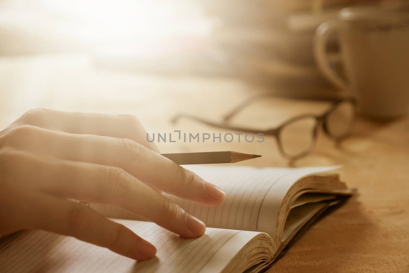 Close up of male hand writing in notebook on wooden desk, Soft focus, Flare sunlight, Vintage tone.