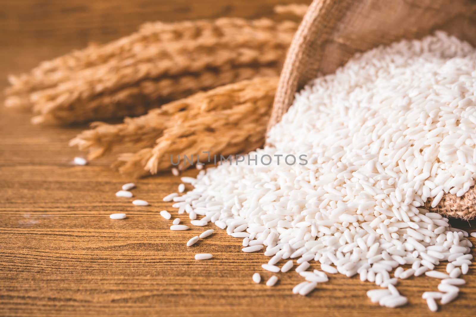 Close up of raw rice in burlap sack on wooden table.