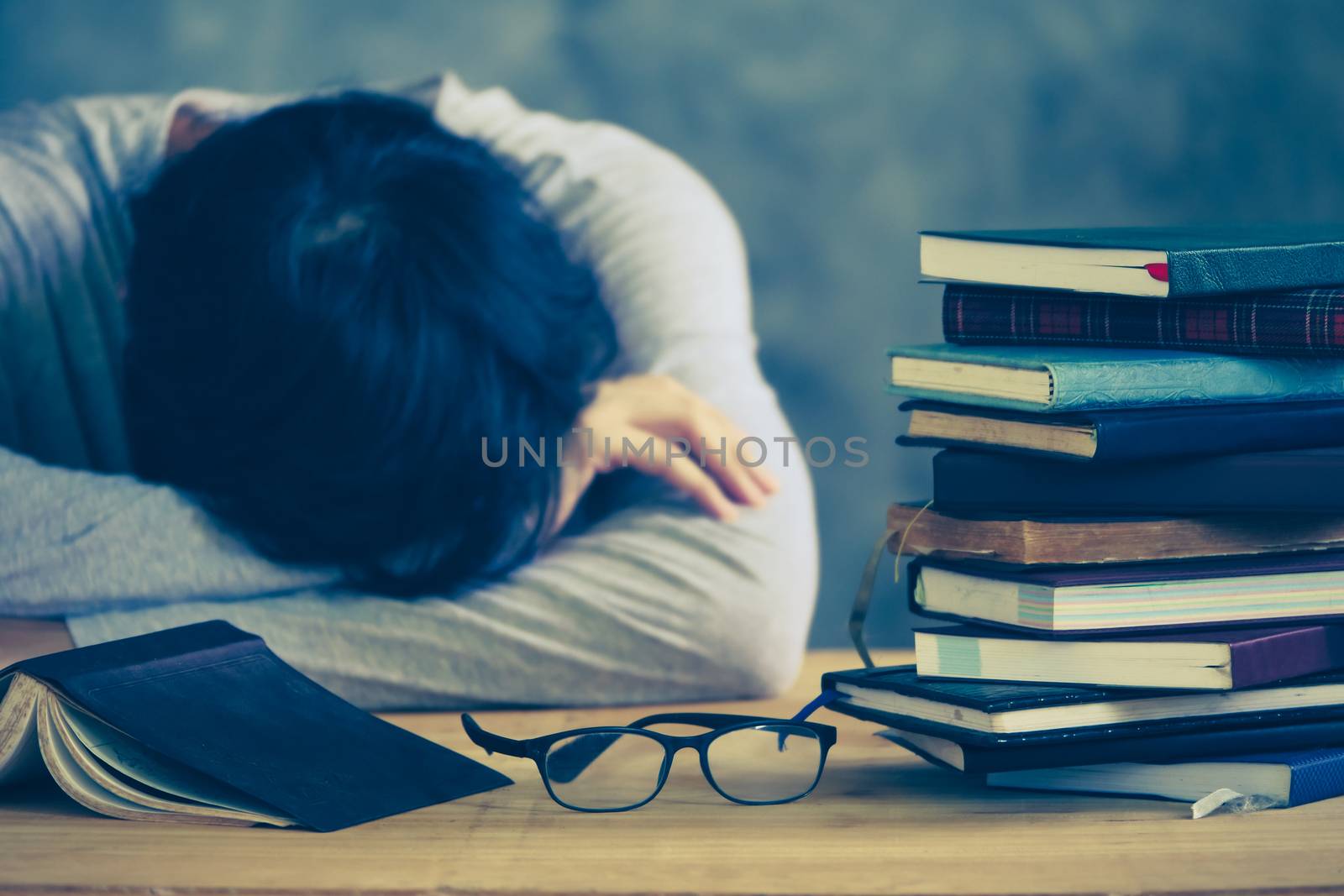 Tired young man sleeping with book stacks on the wooden table. Vintage tone