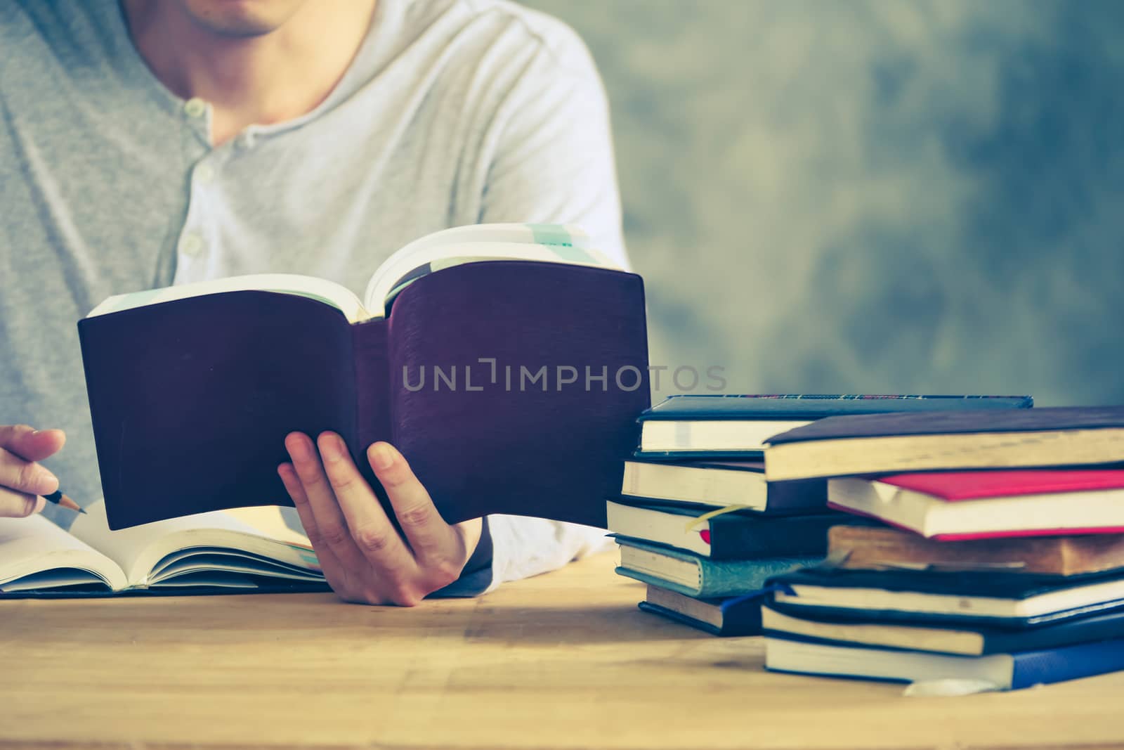 Close up of a man reading a book and making his notes on the wooden table. Vintage tone