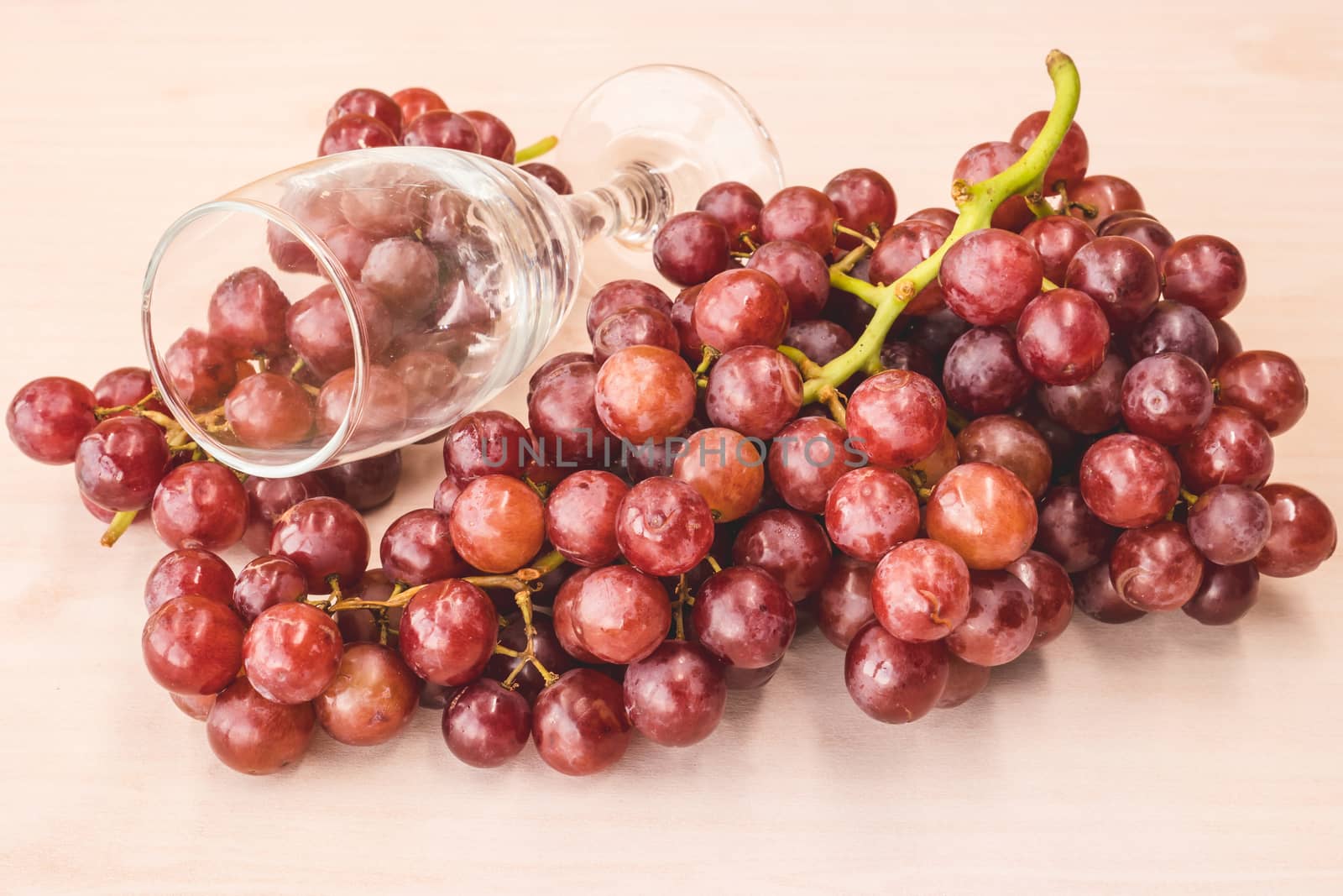 Red grapes with wine glass on the wooden table.