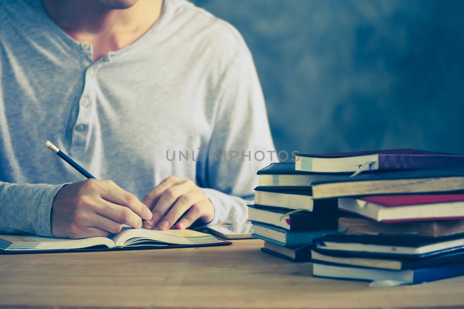 Close up of a man writing in notebook, Stack of old books on wooden desk. Vintage tone