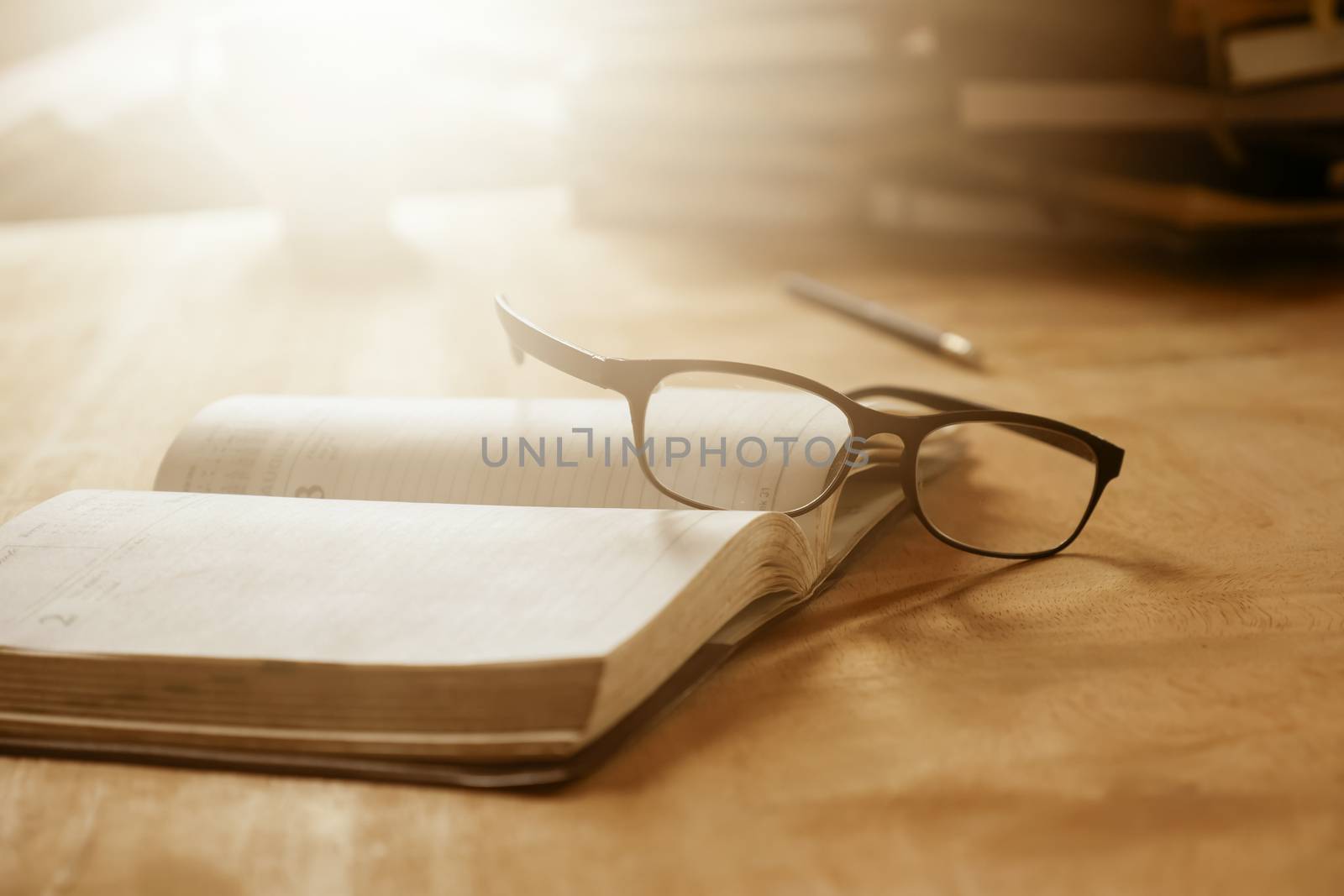 Close up of open notebook with eyeglasses on wooden desk, Soft focus, Flare sun light,Vintage tone.