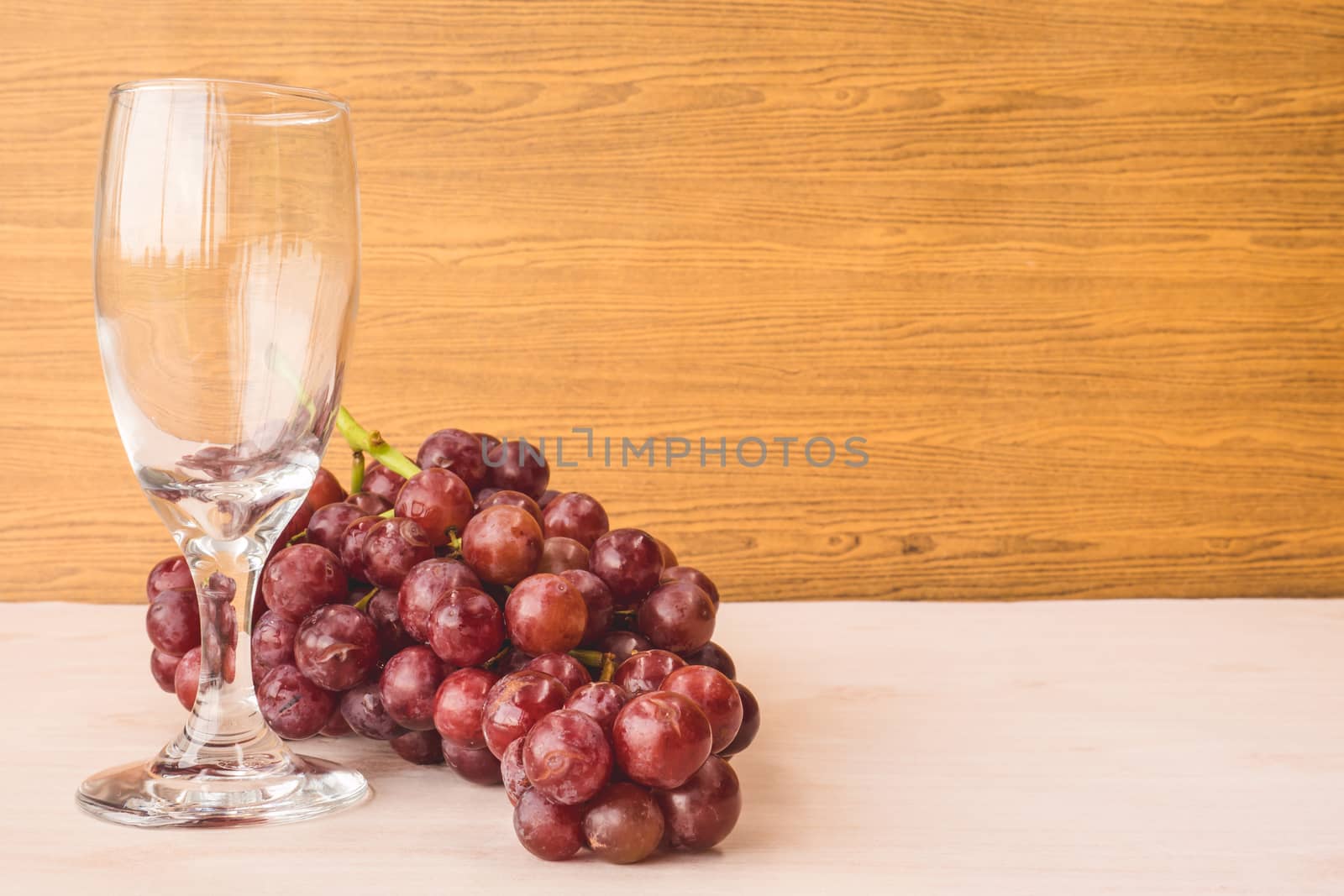 Red grapes with wine glass on the wooden table. Free space for text