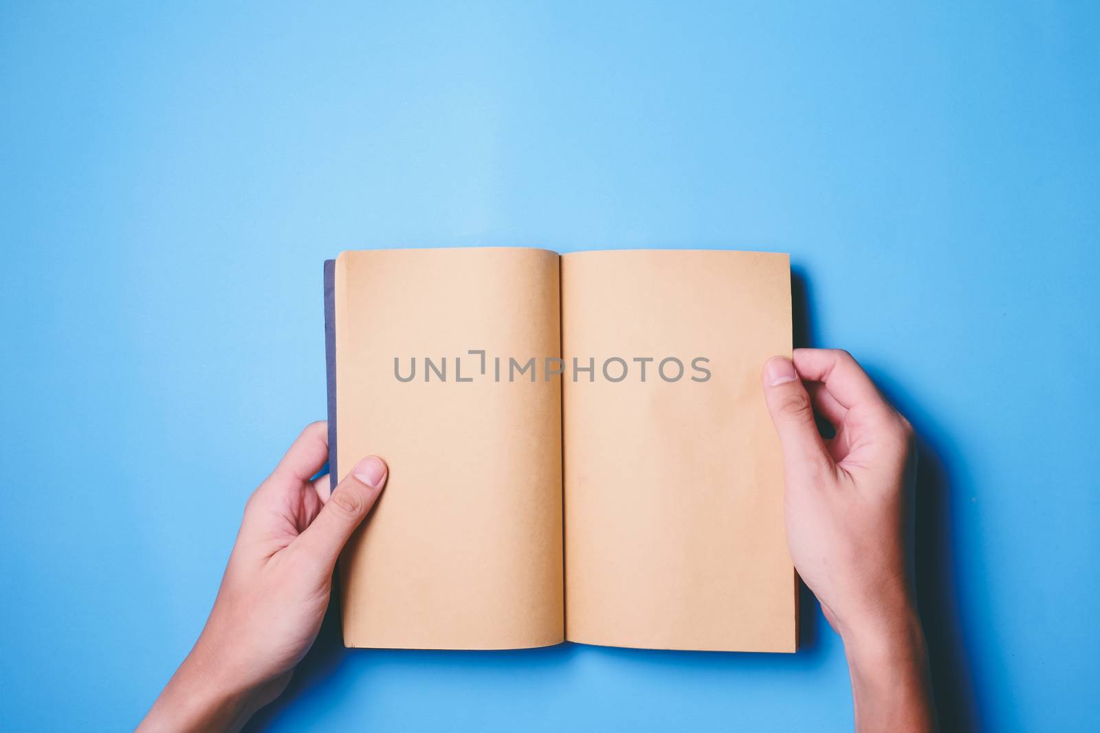 Top view of hands holding a blank book ready with copy space ready for text on blue background.