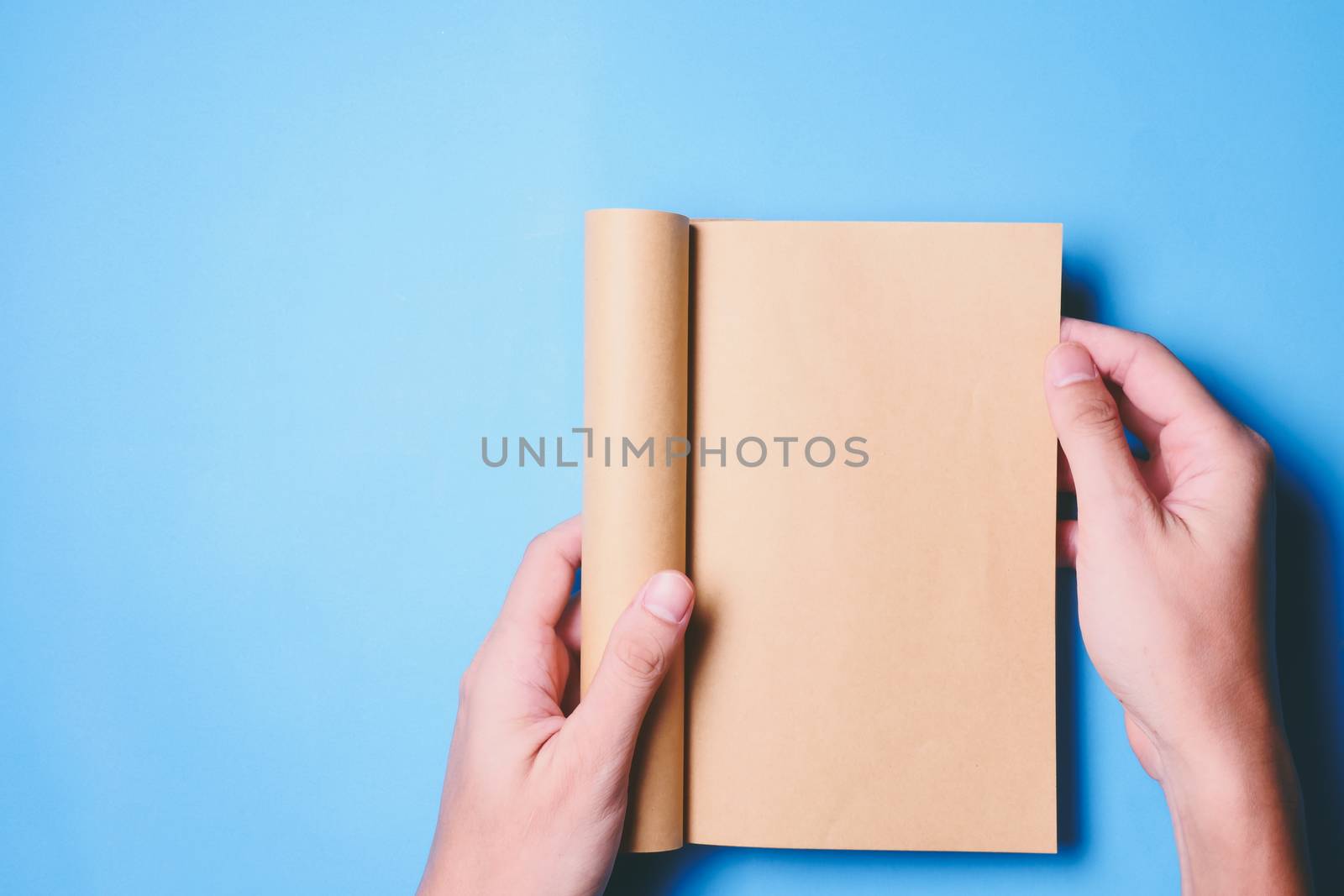 Top view of hands holding a blank book ready with copy space ready for text on blue background.