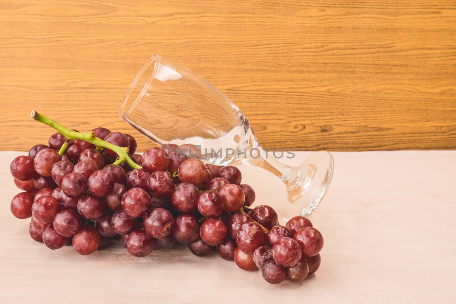 Red grapes with wine glass on the wooden table. Free space for text