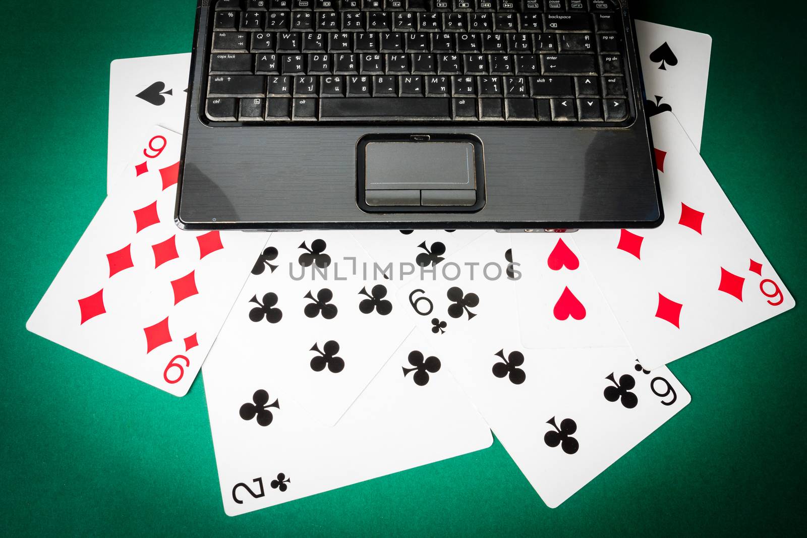 Laptop with playing cards on green background.