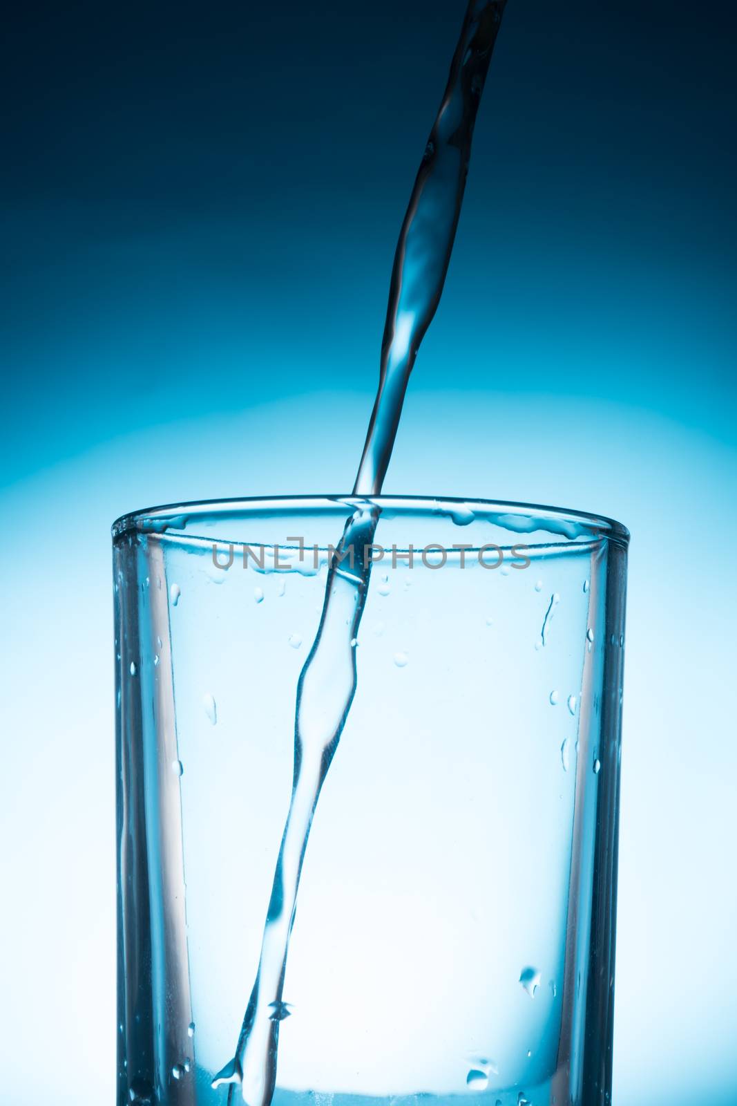 Pouring water into glass on blue background.